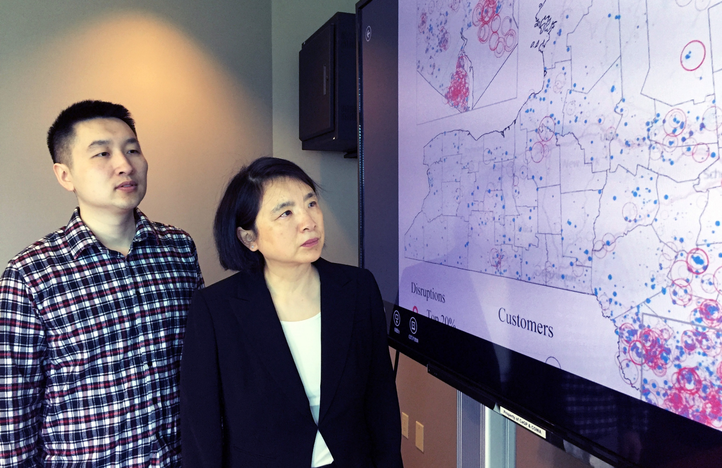 Georgia Tech Ph.D. student Yun Wei and Associate Professor Chuanyi Ji with a map showing utility disruptions in New York State resulting from Super Storm Sandy. (Credit: John Toon, Georgia Tech)